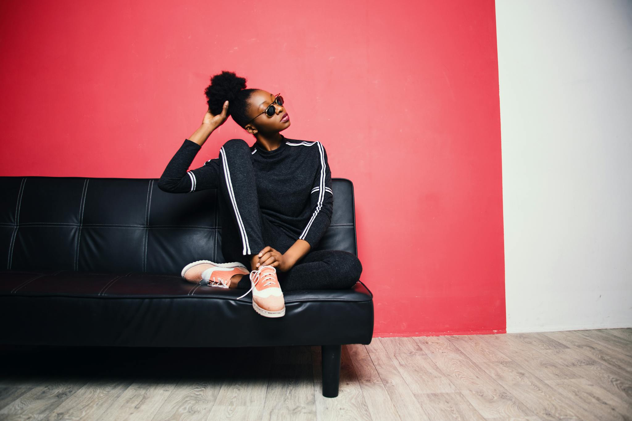 Fashionable young woman in casual wear sitting on a black sofa against a red wall.